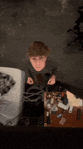 a young man is standing in front of a messy desk and looking at the camera