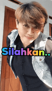 a woman wearing a black shirt and a denim vest stands in front of a door with the words silahkan written on the bottom