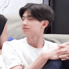 a man in a white shirt is sitting on a couch holding another man 's hands .
