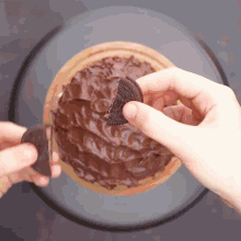 a person is holding an oreo cookie in their hand in front of a chocolate cake