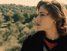 a woman wearing a black and red sweater stands in front of trees