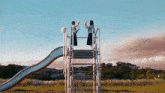two girls standing on top of a slide with their hands in the air