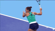 a woman in a green tank top stands on a blue tennis court