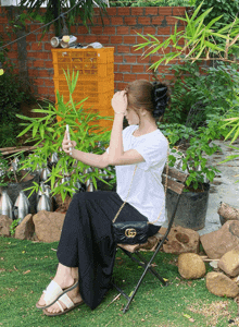 a woman is sitting on a chair taking a picture of a plant