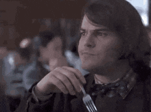 a man in a bow tie is holding a fork in his hand and making a funny face .