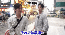two young men are standing on a street with chinese writing on the sidewalk