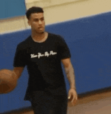 a man in a black t-shirt is holding a basketball on a court .