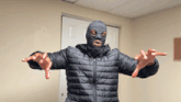 a man wearing a ski mask and a black jacket is standing with his arms outstretched