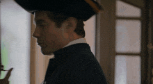 a man wearing a pirate hat and a black suit stands in front of a window