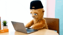 a stuffed animal is sitting at a table using a laptop .