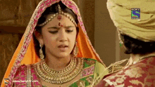 a woman in a pink and orange dress is talking to a man in a green turban on sony tv