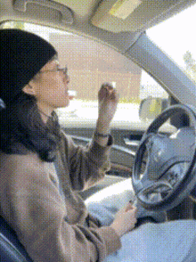 a woman is driving a car and applying lip gloss