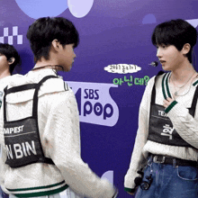 two boys are standing in front of a sbs pop logo