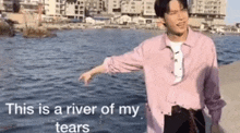 a young man in a pink shirt is pointing at the water .