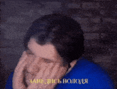 a man in a blue shirt is covering his face with his hands with a caption that says " завелись волося "