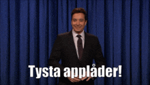 a man in a suit and tie is standing in front of a blue curtain with the words tysta applader in white letters