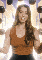 a woman in a brown tank top is smiling in front of a wall of balloons