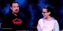 a man and a woman are sitting next to each other in front of a blue background . the woman is wearing glasses .