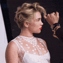 a woman in a white dress has her hair styled by a man
