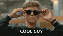 a young man is wearing sunglasses and the words `` cool guy '' are on the bottom .