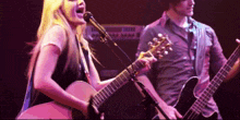 a woman singing into a microphone while a man plays guitar