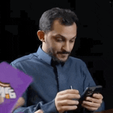 a man in a blue shirt and tie is sitting at a table looking at his cell phone .