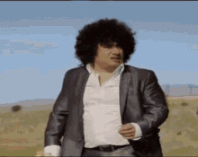 a man with curly hair is wearing a suit and a white shirt and is standing in a field .
