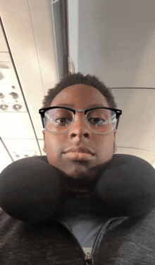 a man wearing glasses and a neck pillow