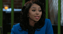 a woman with curly hair is wearing a blue jacket and a pink shirt while sitting at a table .