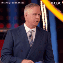 a man in a suit and tie stands in front of a sign that says familyfeud canada