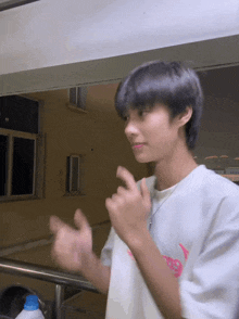a young man wearing a white t-shirt with a pink logo on the front is giving a thumbs up