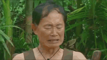 a man is crying in the jungle while wearing a tank top and a necklace .