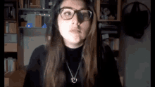 a woman wearing glasses and a black turtleneck looks at the camera