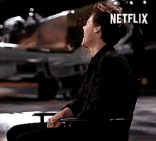 a man is sitting in a chair and laughing with the word netflix on the bottom .