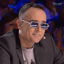 a man wearing sunglasses and a suit is sitting in front of a microphone with the word talent on the bottom