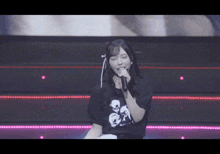 a girl singing into a microphone wearing a shirt with skulls on it