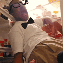 a man wearing glasses and a bow tie is reaching into a fridge
