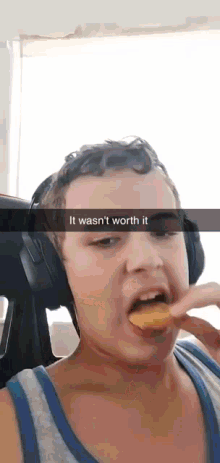 a young boy wearing headphones is eating a chip with the caption " it wasn 't worth it "