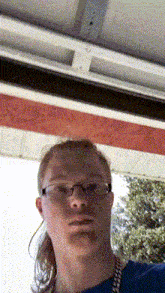 a man wearing glasses and a blue shirt is standing in front of a red and white sign