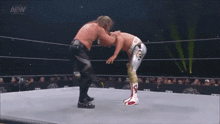 two wrestlers are fighting in a wrestling ring while a referee stands behind them .