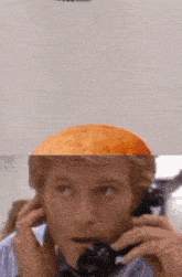 a man talking on a phone with a bun on his head behind him