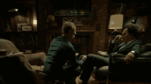 two men are sitting on a couch and one is kneeling down