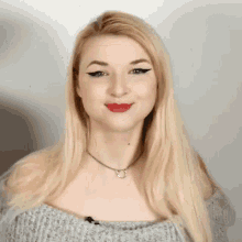 a blonde woman wearing a grey off the shoulder top and a necklace