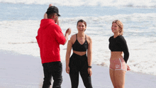 a man in a red hoodie is taking a picture of two women on a beach