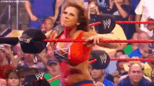a female wrestler is standing in a wrestling ring holding a rope in front of a crowd .