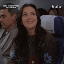 a woman is smiling on an airplane while watching hulu mid century modern