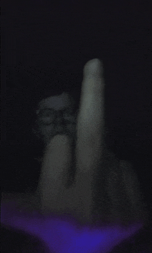 a person wearing glasses is giving the middle finger in the dark