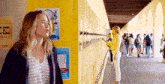 a girl is standing in front of a yellow locker in a hallway .