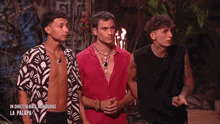 three men are standing next to each other in a jungle . one of the men is wearing a red shirt .