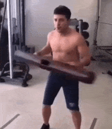 a shirtless man is standing in a gym holding a large wooden plank .